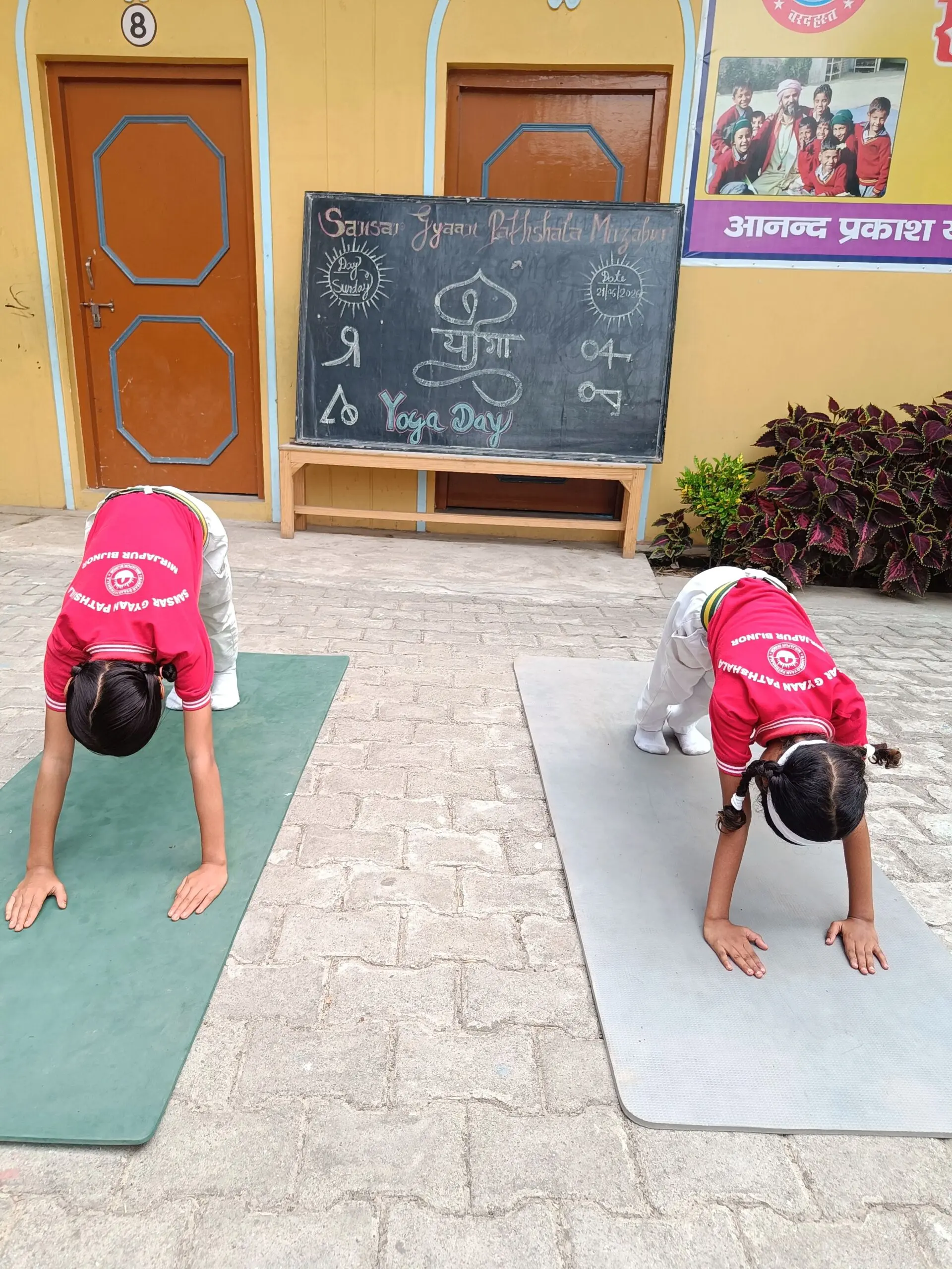 Students practicing a forward bend near the Yoga Day chalkboard